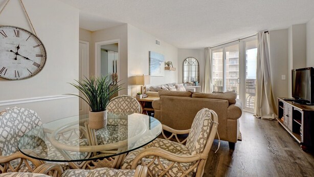 A living room with a round glass table, wicker chairs, a sofa, a television, and a large wall clock. - 2 bedroom,  modern oceanfront condo (North Topsail Beach)