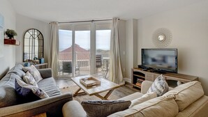 A living room with a sofa, a coffee table, a TV, and a balcony with a view of a building. - 2 bedroom,  modern oceanfront condo (North Topsail Beach)