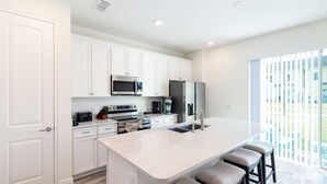 A modern kitchen with white cabinetry, stainless steel appliances, and a large island with bar stools. - Margaritaville Townhome Retreat (Kissimmee)