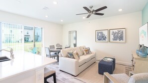 A modern living room with a white sofa, a dining area, and a kitchen with a white countertop. - Margaritaville Townhome Retreat (Kissimmee)