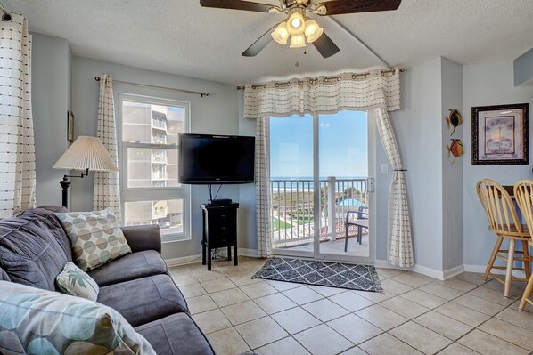 A living room with a sofa, TV, and a balcony with a view.