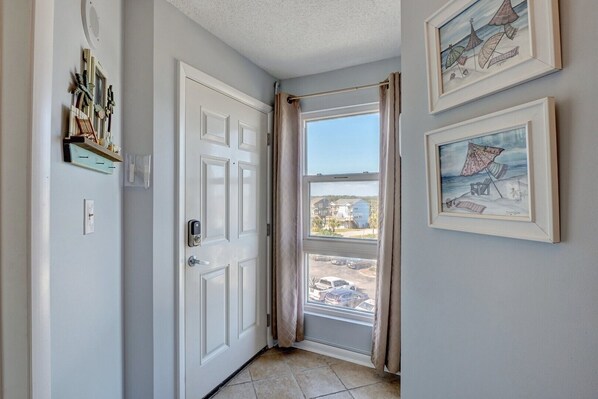 A hallway with a white door, a window with curtains, and two framed artworks on the wall.