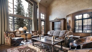 Un amplio salón con muebles de cuero, ventanas grandes y vista a árboles.