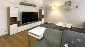 A modern living room with a flat-screen TV, wooden shelving, a white coffee table, and a gray sofa. - Mein Apartment, Stars for 4 Person (Frankenthal)