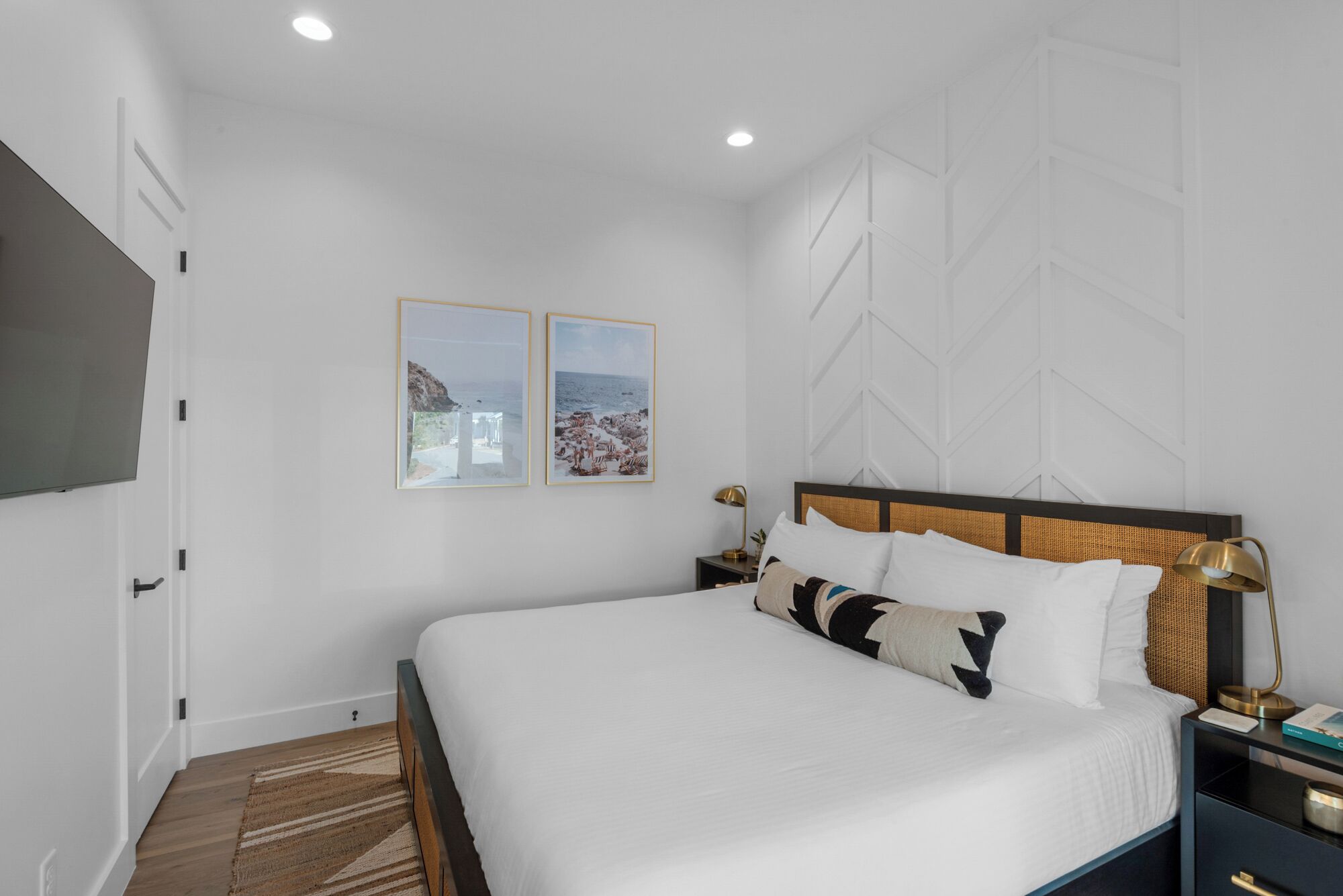 Un dormitorio moderno con una cama grande, dos mesitas de noche y un televisor montado en la pared.