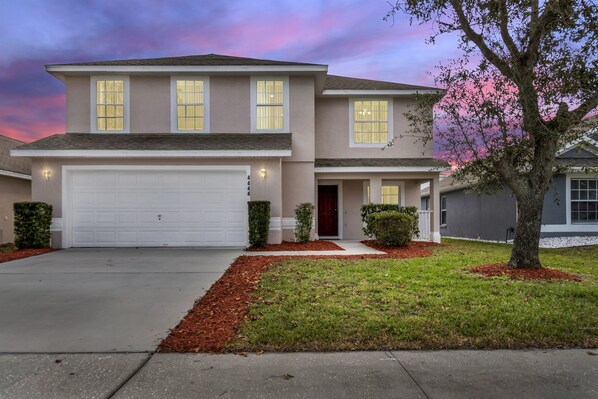 A two-story house with a garage, a front porch, and a well-maintained lawn. - 4BR | South Facing Pool | Close to Attractions (Kissimmee)