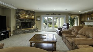 A living room with a stone fireplace, a television, a brown leather couch, and a coffee table.