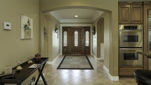 A hallway with a dark rug, a wooden bench, and a double oven in the kitchen area.
