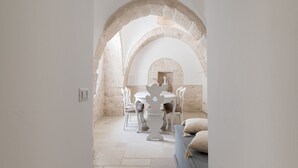 A dining area with a stone archway, a round table, and white chairs. - Trulli Julia con Piscina by Wonderful Italy (Martina Franca)