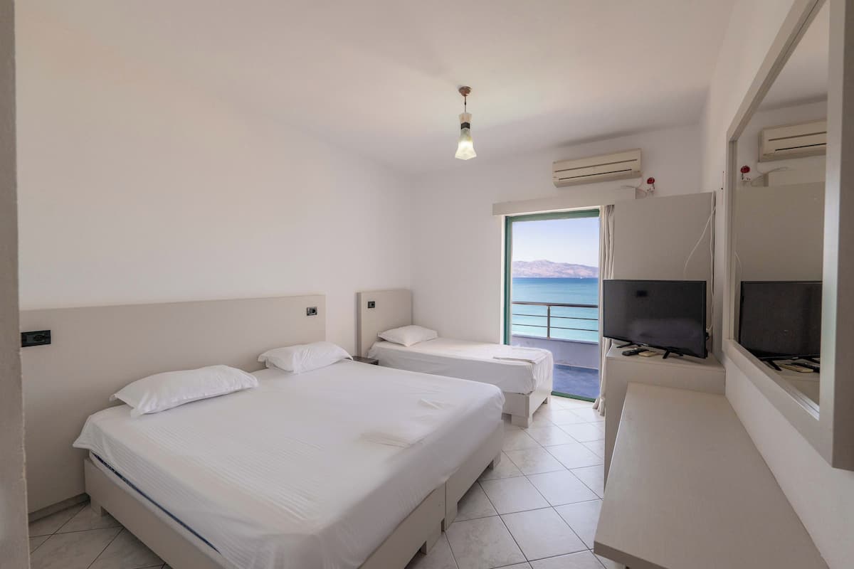 A hotel room with two beds, a television, and a view of the sea.