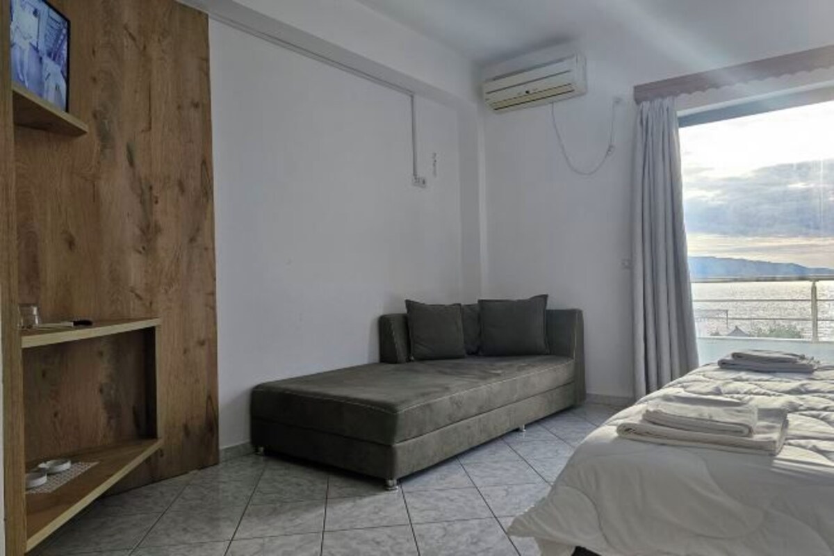 Un dormitorio con sofá cama, repisa de madera, cama con toallas dobladas y vistas al exterior.