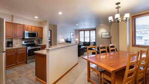 A modern kitchen with wooden cabinets, a central island, and a dining area with a wooden table and chairs. - Family Ski Condo With Continental Divide View - Zephyr Mountain Lodge Value-rated 2508 3 Bedroom Condo (Winter Park)
