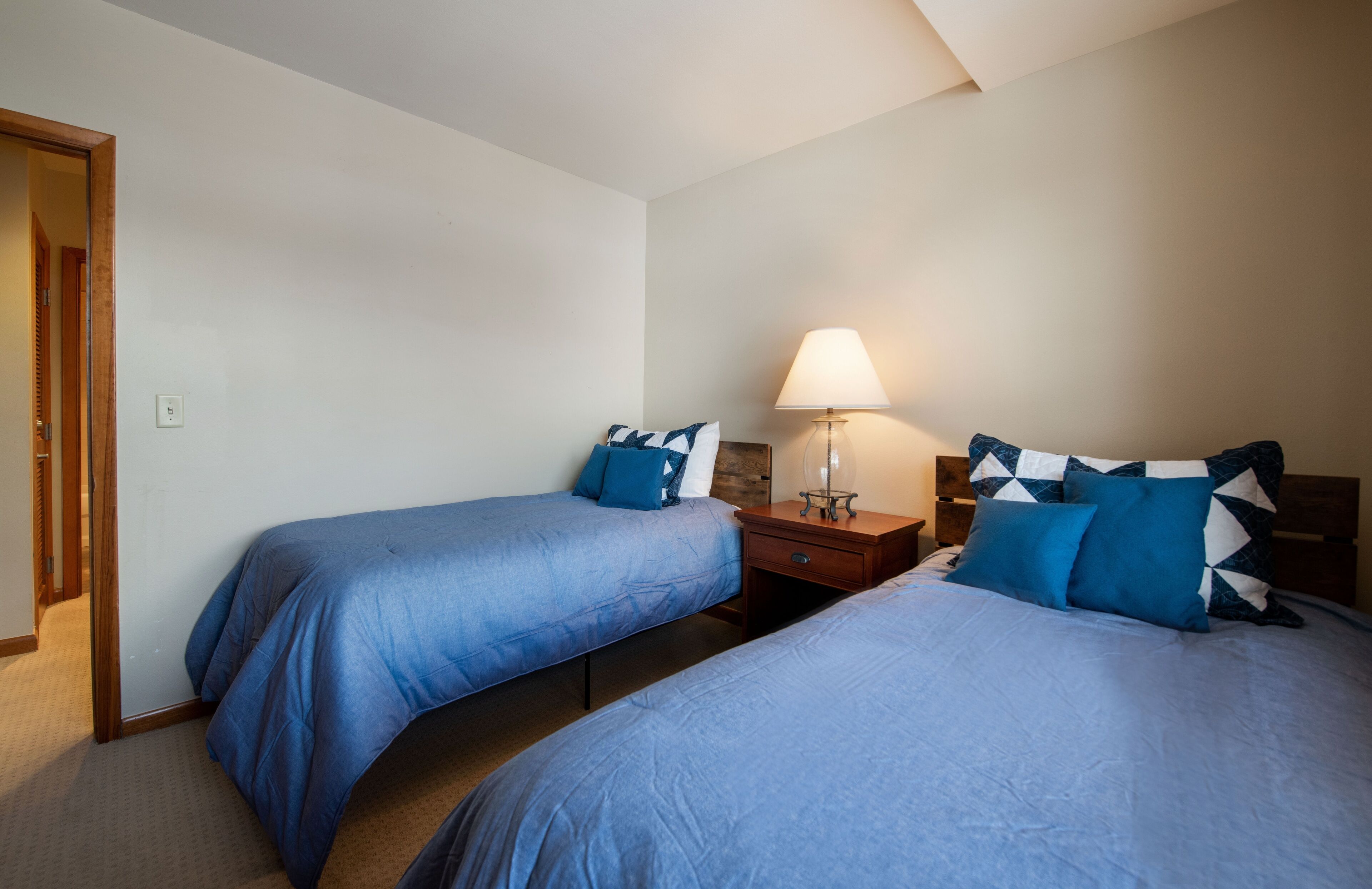 A bedroom with two single beds, a nightstand with a lamp, and a wooden door.