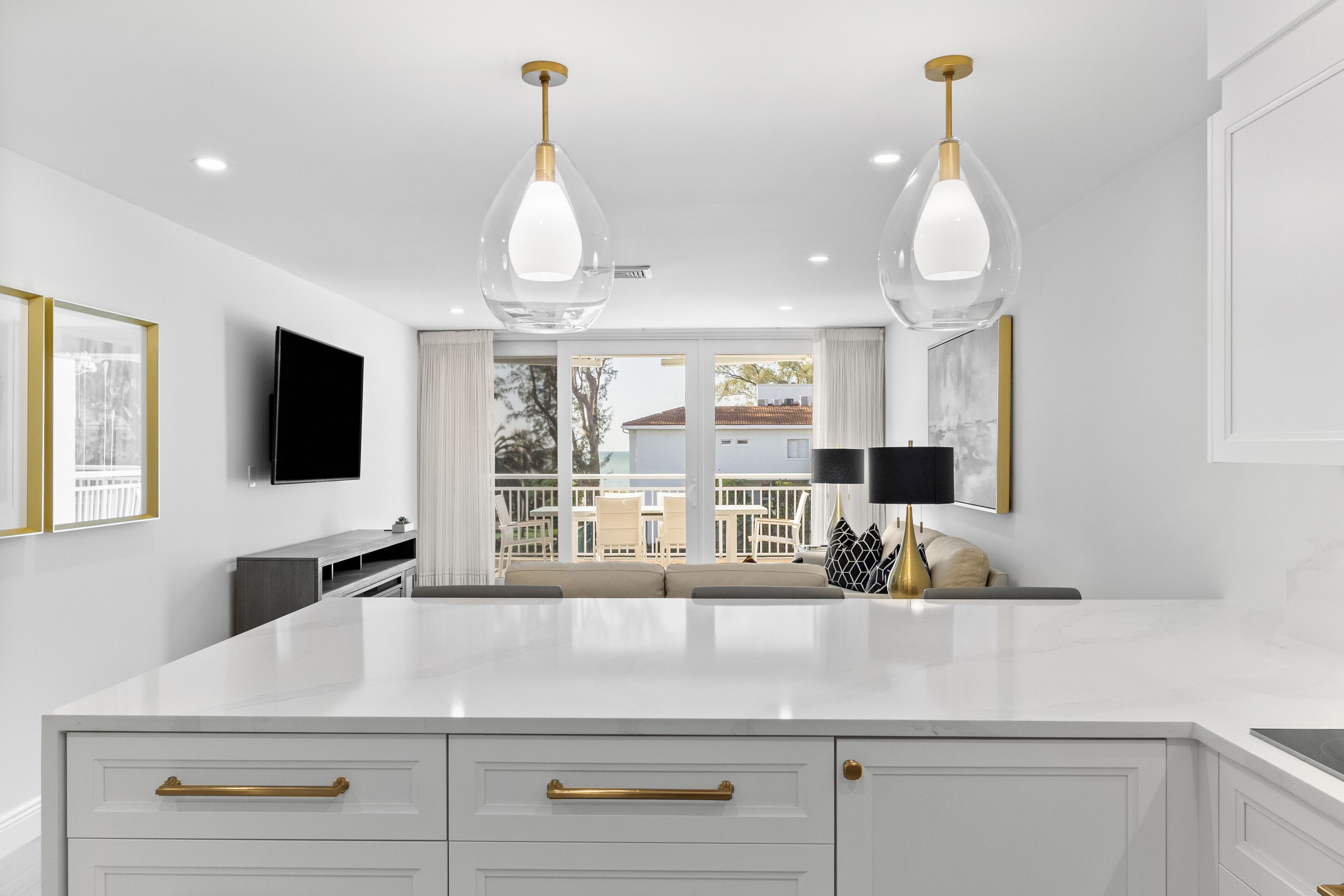 A modern kitchen with white cabinetry, gold handles, and pendant lighting.
