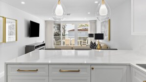 Una cocina moderna con armarios blancos, tiradores dorados e iluminación colgante.