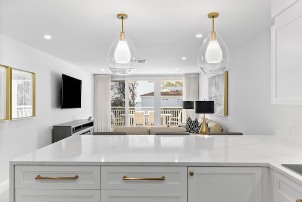 A modern kitchen with white cabinetry, gold handles, and pendant lighting.