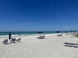 A beach with sun loungers and umbrellas, a clear sky, and the ocean.