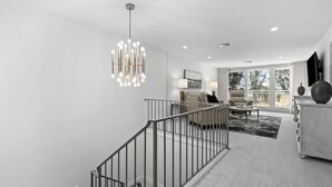 Un interior moderno con una escalera, una sala de estar con sofá y mesa de centro, y un balcón con barandilla.