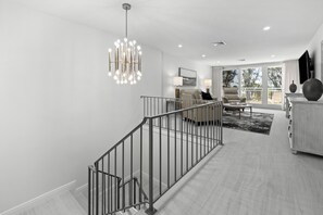 Um interior moderno com escada, sala de estar com sofá e mesa de centro, e varanda com guarda-corpo.