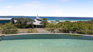 Une piscine aux eaux cristallines, avec vue sur l’océan et un bâtiment en arrière-plan.