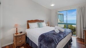 Une chambre à coucher avec un grand lit, une table de chevet, une lampe et une vue sur l’océan par la fenêtre.