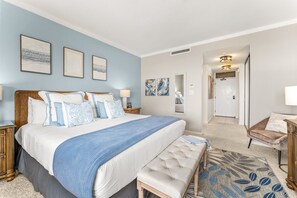 Een slaapkamer met een groot bed, nachtkastjes, een bankje en kunstwerken aan de wanden.