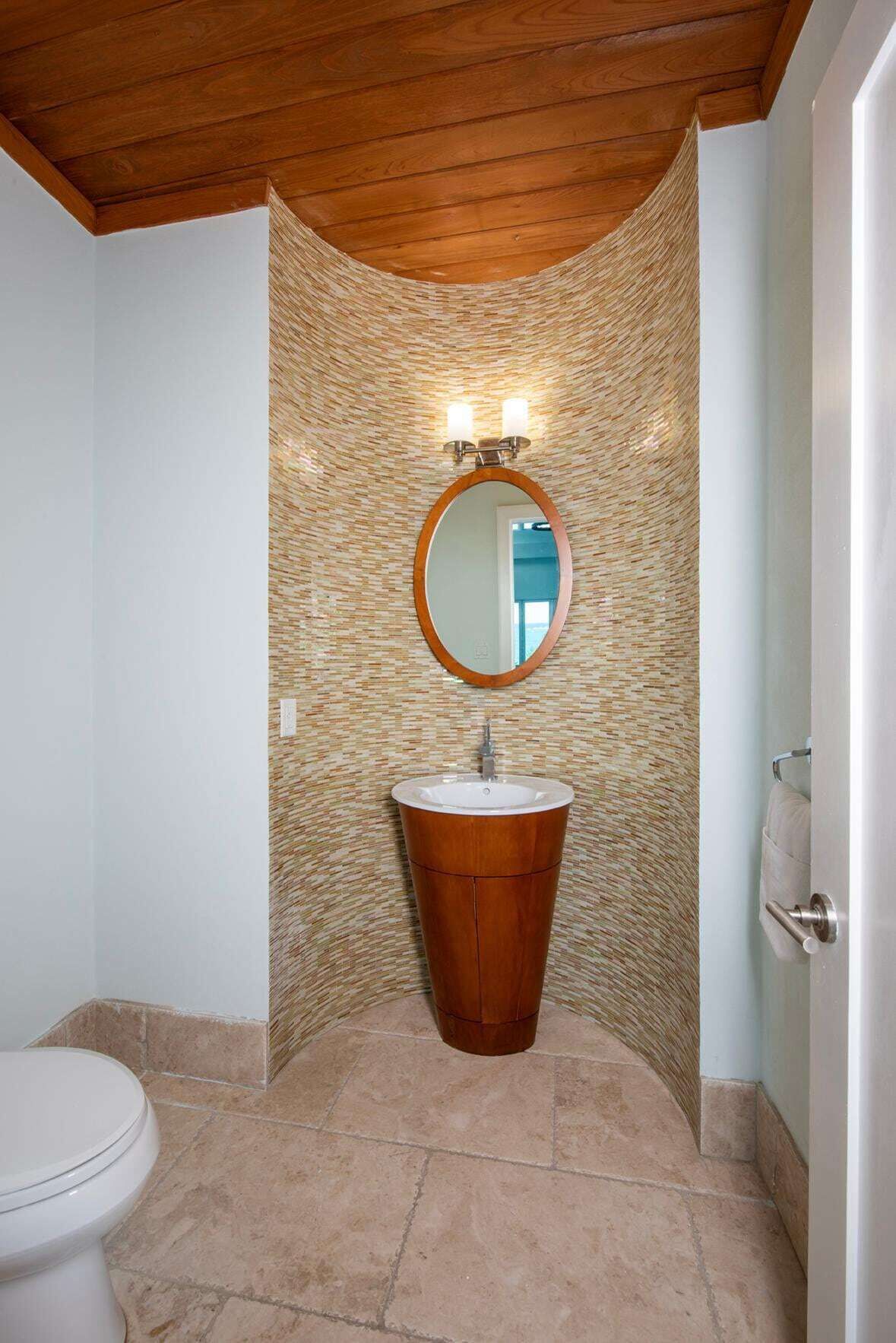 A bathroom with a wooden ceiling, a round mirror, a wooden sink, and a toilet.