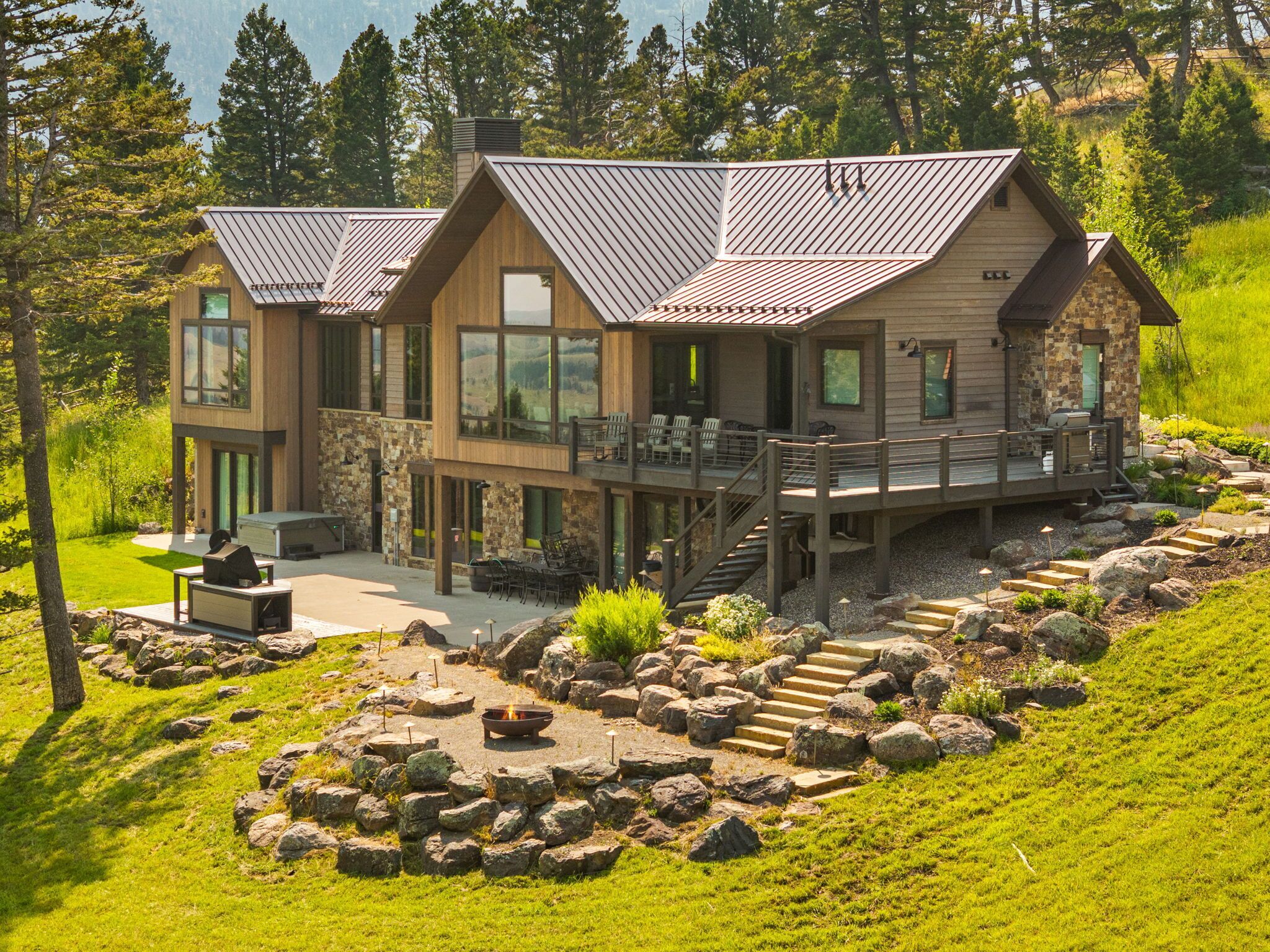 A modern two-story lodge with a deck, stone walls, and a fire pit area.