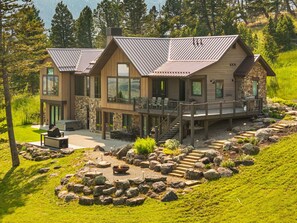 A modern two-story lodge with a deck, stone walls, and a fire pit area. - Elk Haven Ranch-Gorgeous home in Bridger Canyon on 100+ acres with a hot tub (Bozeman)