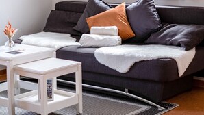 Un salon moderne avec un canapé gris foncé, une table d’appoint blanche et une fenêtre avec des rideaux.