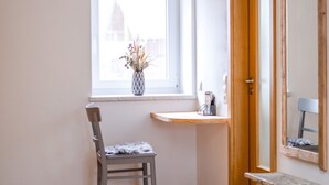 Une pièce dotée d’une lucarne, d’un bureau en bois, d’une chaise, d’un petit tabouret et d’un miroir.