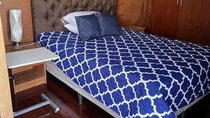 Un dormitorio con una cama grande, cabecera de madera, mesita de noche con lámpara y un armario.
