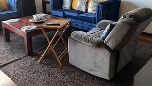 Una sala de estar con un sofá azul, un sillón gris, una mesa de centro de madera y un cuadro en la pared.