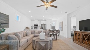 Un salon spacieux avec un grand canapé d’angle, une table basse et un ventilateur de plafond.
