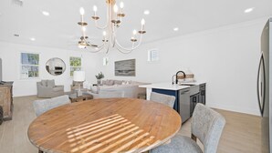 Une cuisine moderne dotée d’un îlot central, un coin repas avec une table ronde en bois, et un espace de vie comprenant un canapé et un téléviseur.