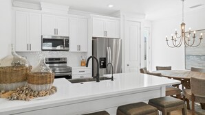 Une cuisine moderne avec des meubles blancs, des appareils en acier inoxydable, un grand îlot central et un coin repas agrémenté d’un lustre.