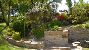 Una estructura de piedra con escalones que conducen a un muro de piedra, rodeada de abundante follaje y árboles.