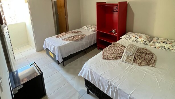 A room with two beds, a red wardrobe, a small table, and a door leading to an outdoor area. - Pousada Mar do Sonho Praia (Ipojuca)