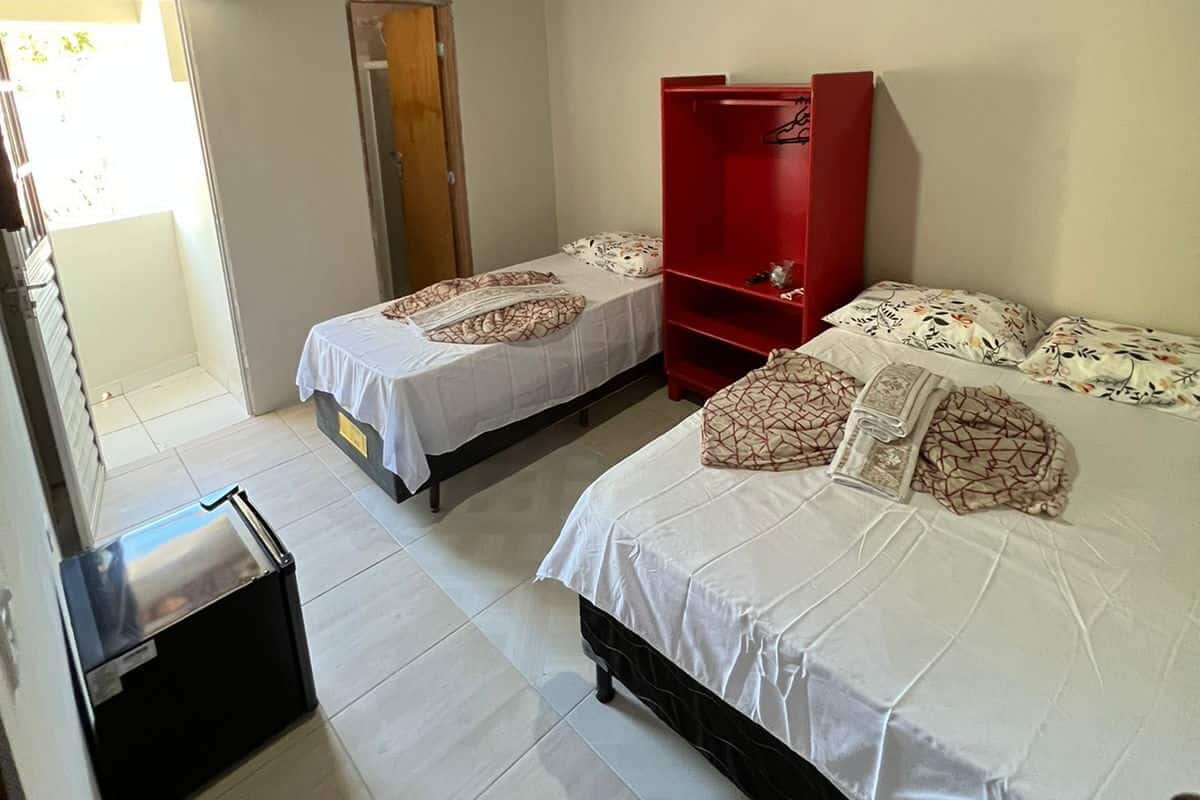 Ein Zimmer mit zwei Betten, einem roten Kleiderschrank, einem kleinen Tisch und einer Tür zu einem Außenbereich.