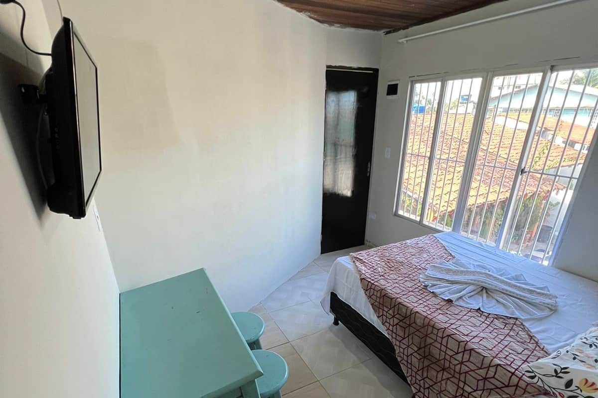 Ein kleines, sauberes Zimmer mit einem Bett, einem Schreibtisch und einem an der Wand befestigten Fernseher.
