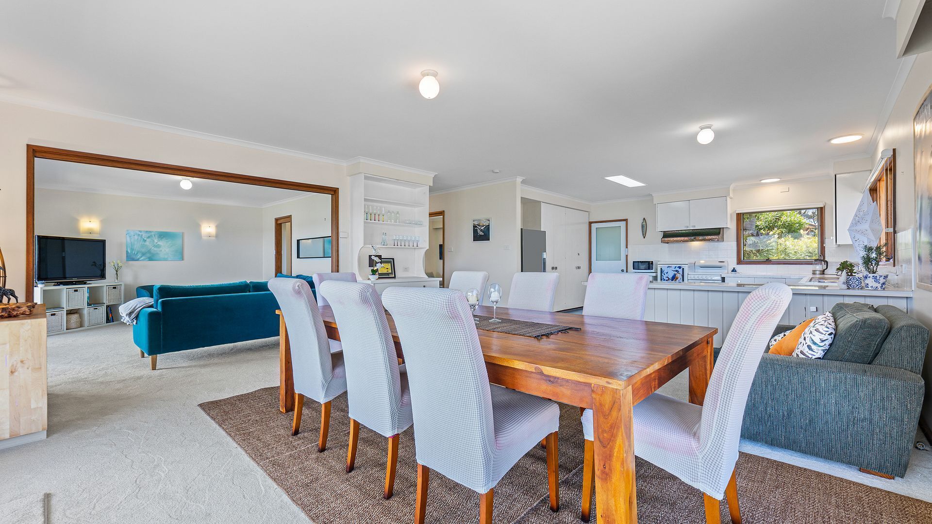 A spacious living area with a dining table, chairs, a sofa, and a kitchen in the background.