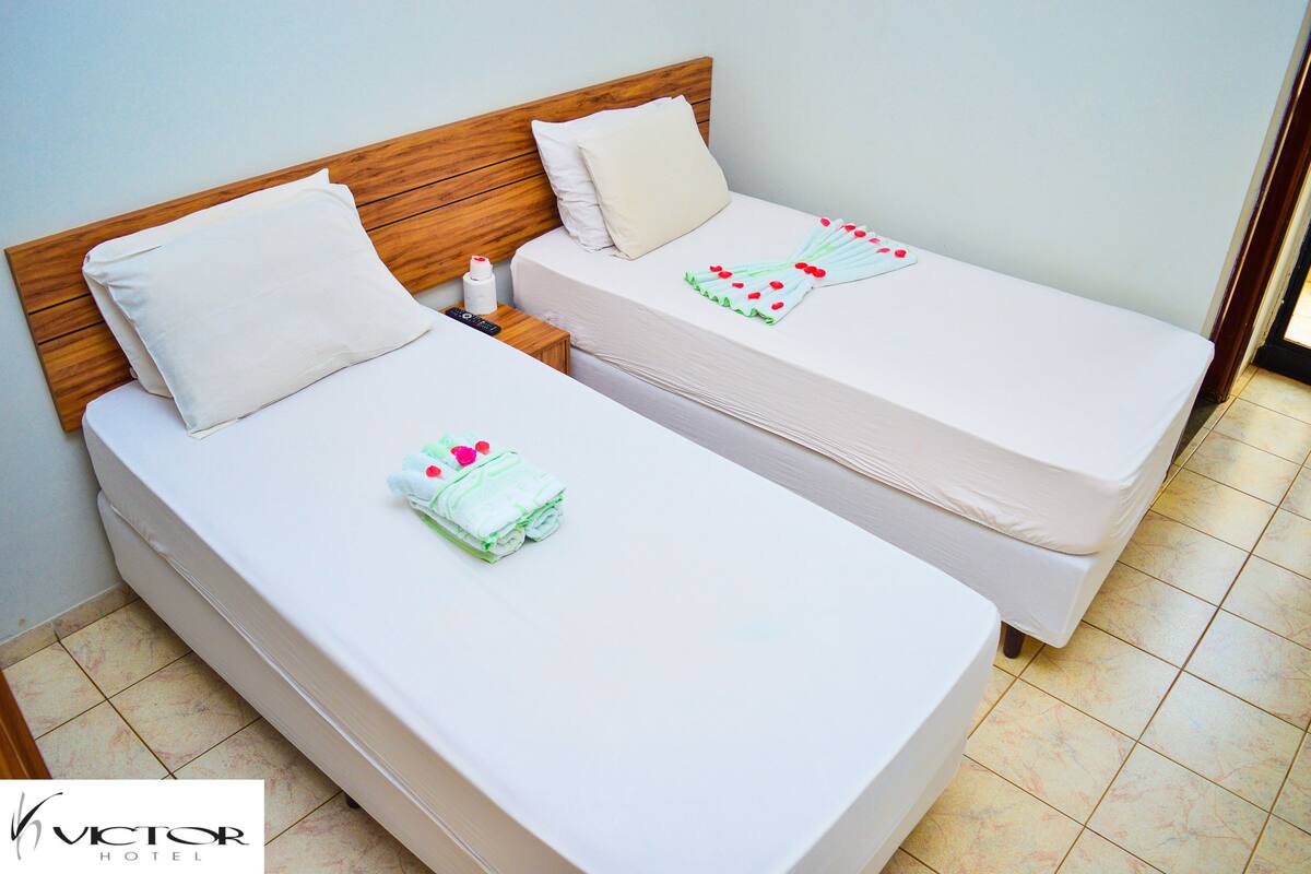 Two single beds with wooden headboards, white bedding, and a remote control on the nightstand.