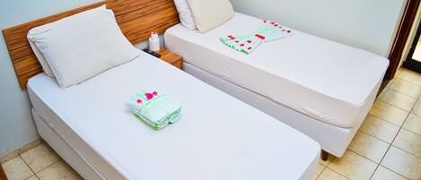 Dos camas individuales con cabeceros de madera, ropa de cama blanca y un control remoto en la mesita de noche.
