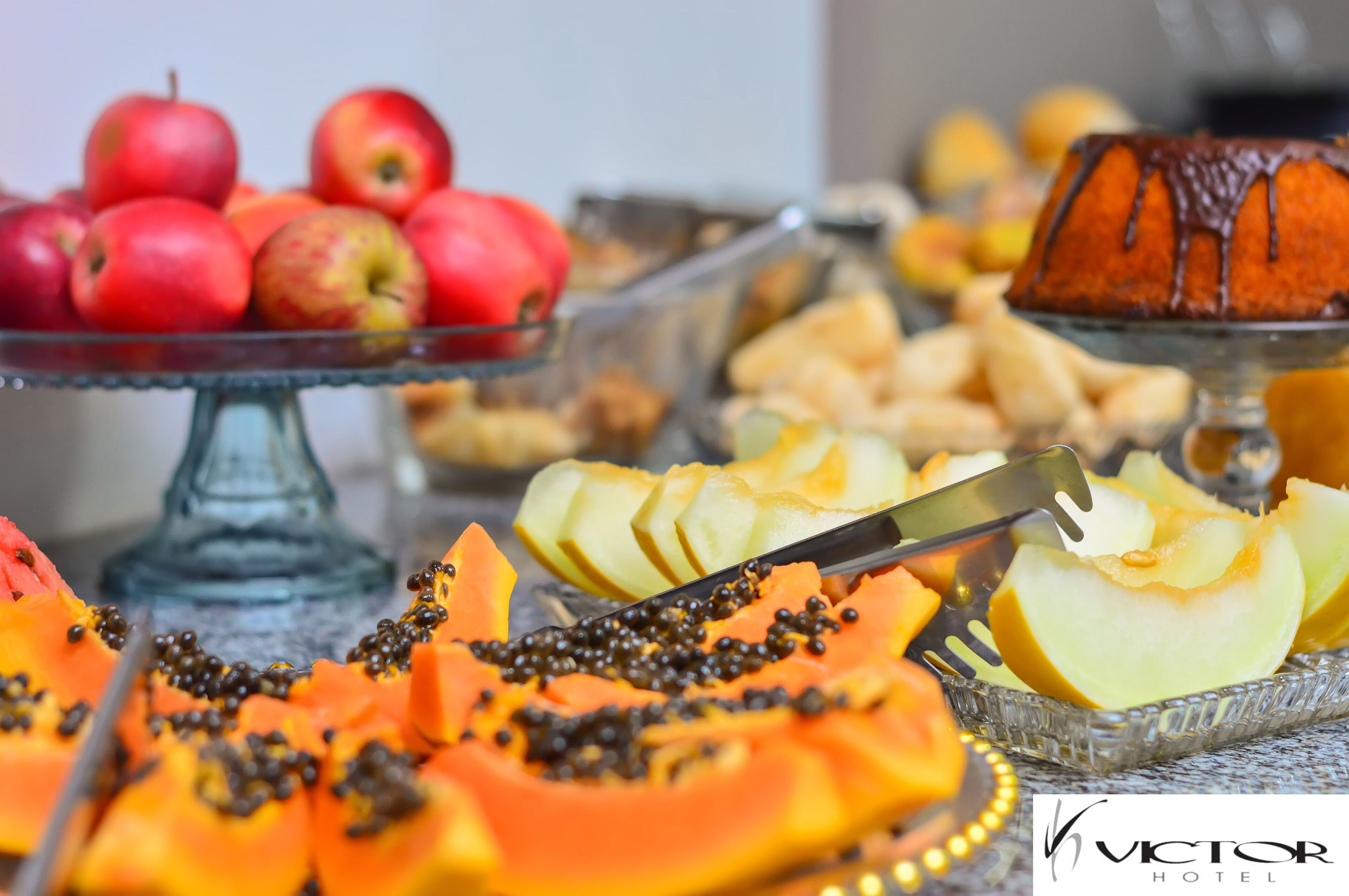 A buffet with various fruits and desserts, including apples, papaya, and a bundt cake.
