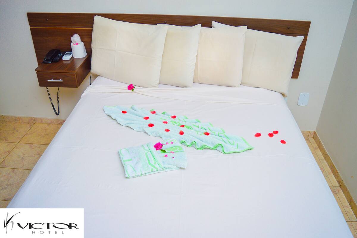 A hotel room with a neatly made bed, a bedside table with a phone and a tissue box, and a wall socket.