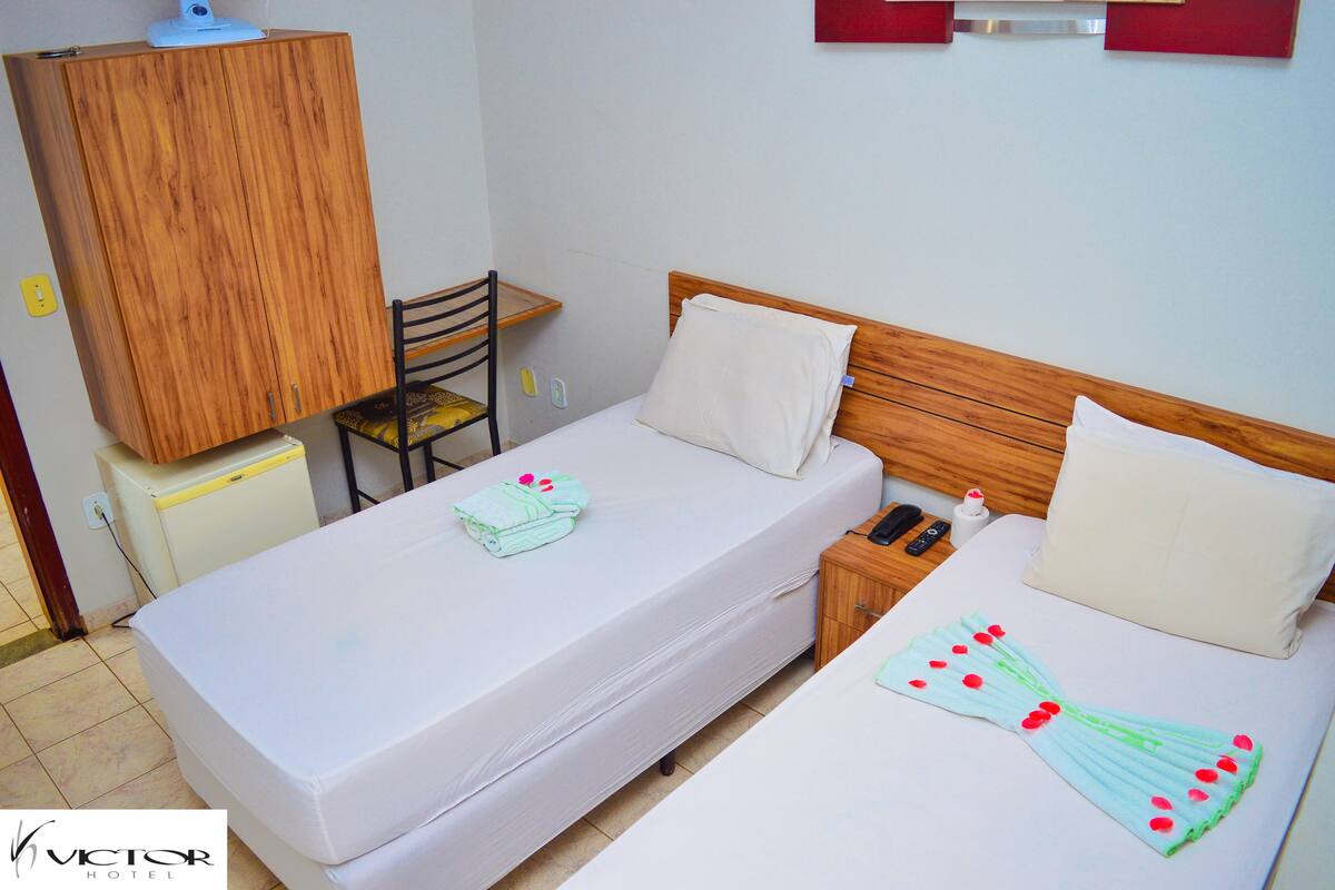 A hotel room with a bed, a wooden wardrobe, a desk, and a chair.