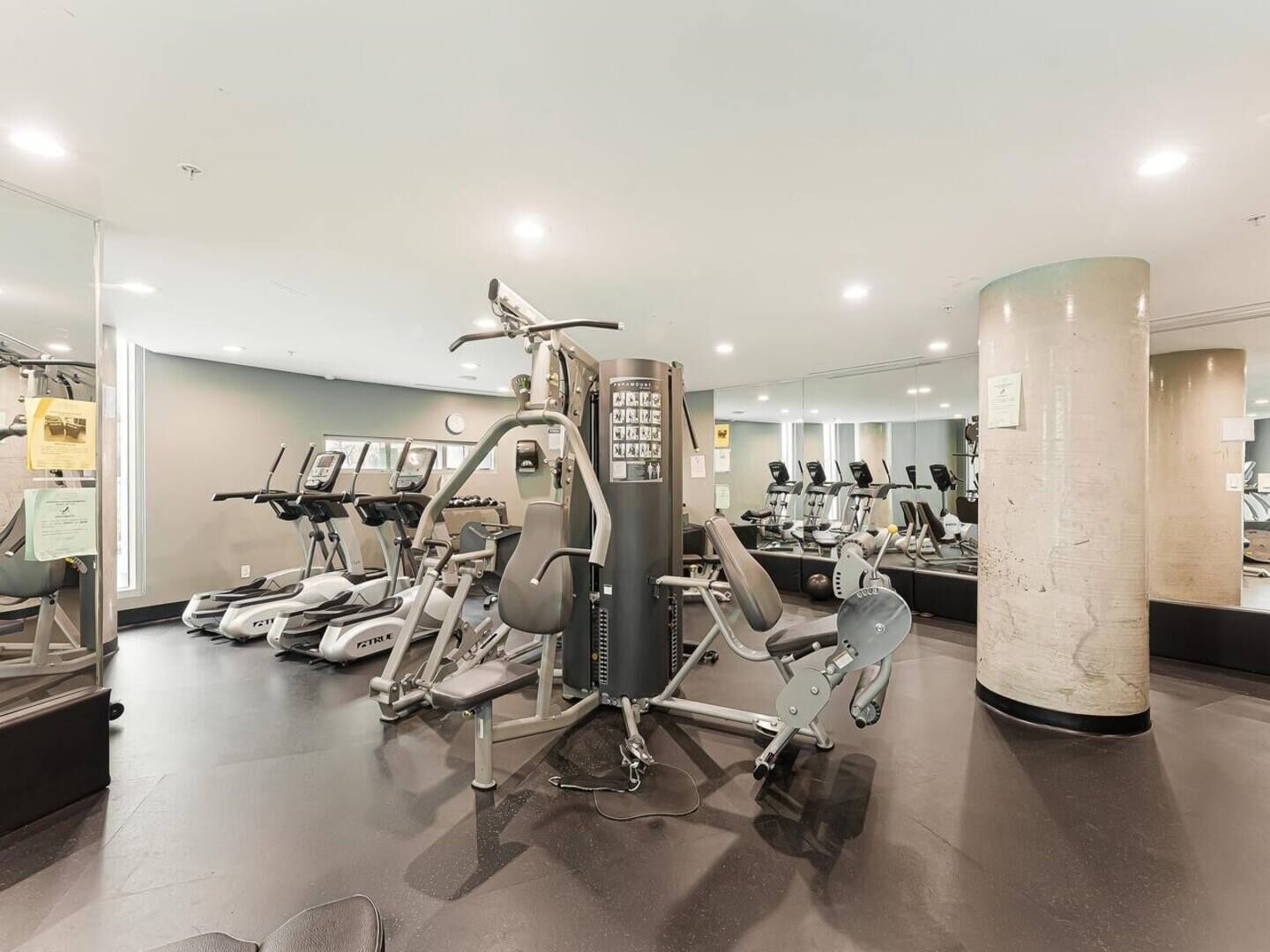 Ein modernes Fitnessstudio mit verschiedenen Trainingsgeräten, einer großen Spiegelwand und einem glatten Boden.