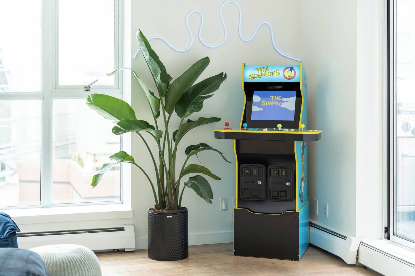 A room with a large potted plant, a Simpsons arcade machine, and a view through a window.