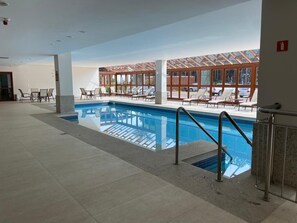 En indendørs swimmingpool med glasvægge, liggestole og flisegulv.