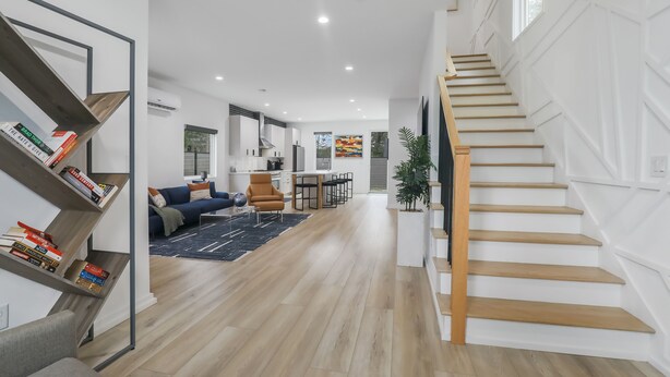 A modern interior with a staircase, a living area with a sofa and coffee table, and a kitchen in the background. - Modern Home with Rooftop Deck (Atlanta)